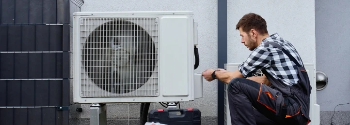 HVAC technician servicing an outdoor heat pump condenser unit beside a residential building.