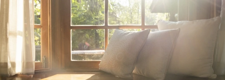 Sunlight streaming through a large window, illuminating decorative pillows on a cozy indoor window seat.